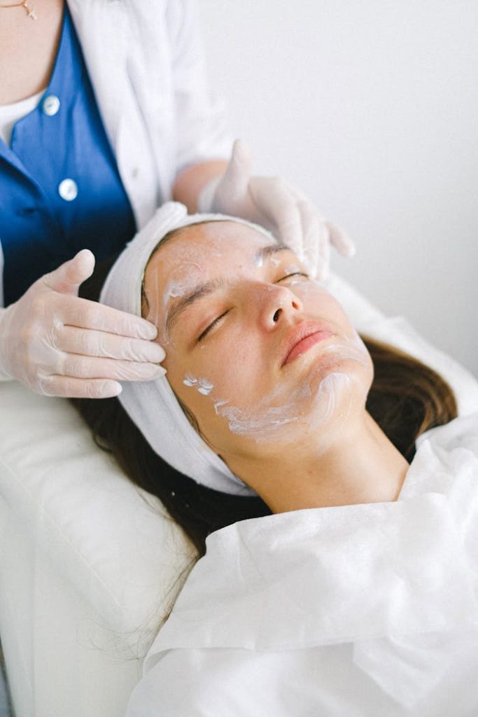 crop-beautician-massaging-client-face-with-lotion-during-spa-procedures-5069493 Woman receiving a facial treatment at a spa, promoting skin health and relaxation.